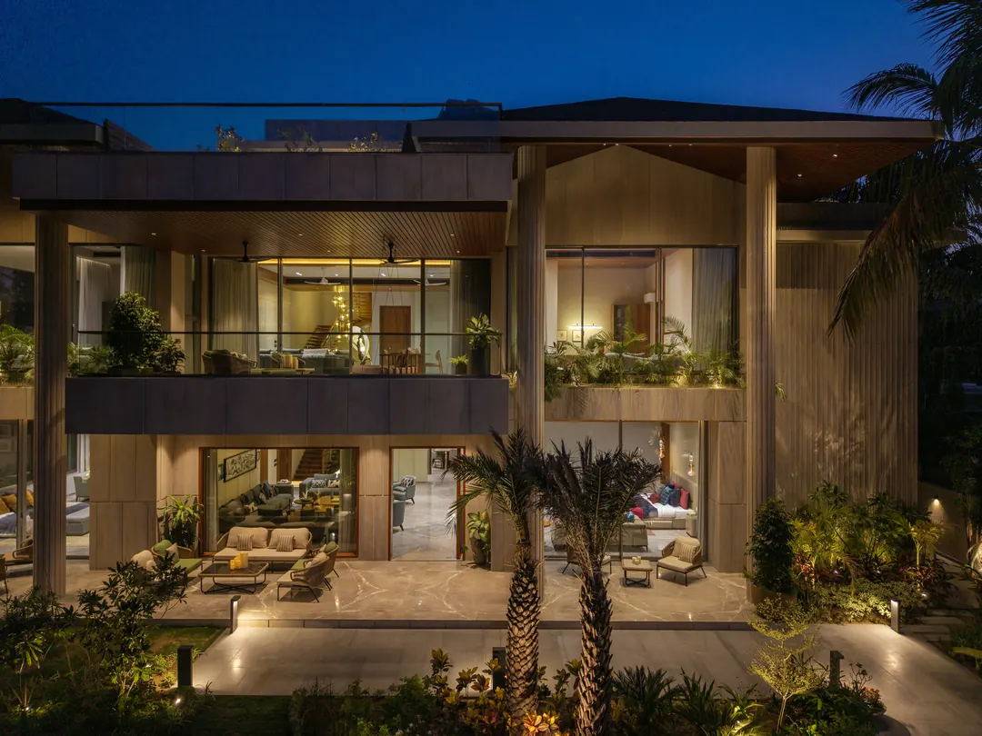 A two-storey house at blue hour, lit from within, palms along the terrace.