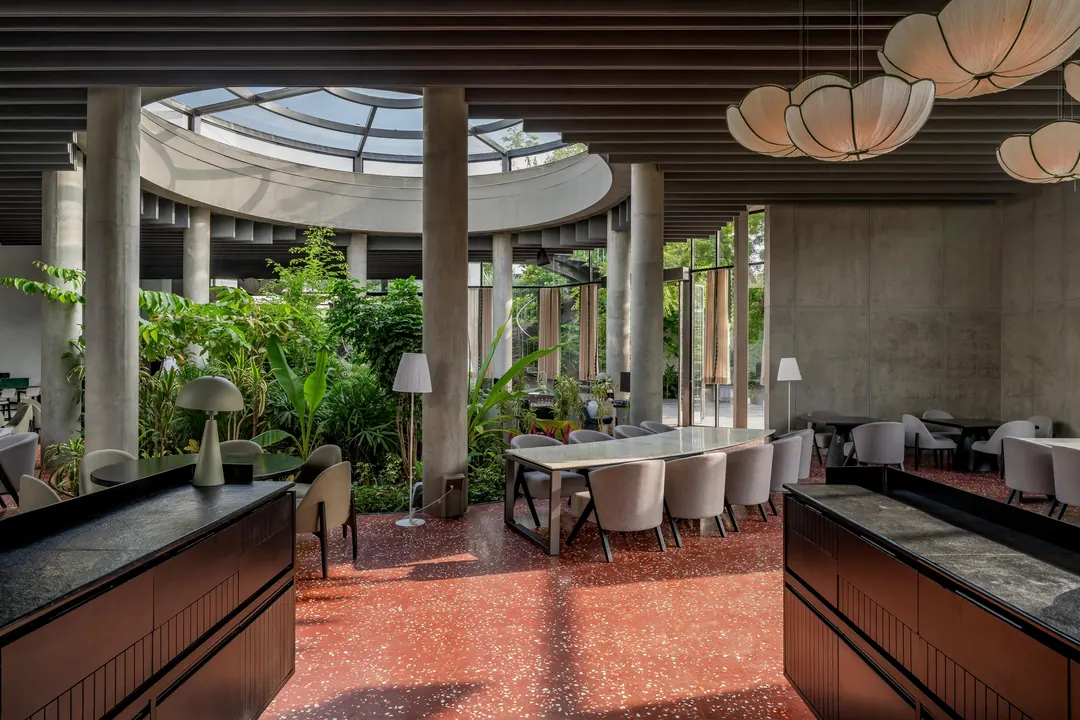 A dining hall under a ring skylight: paper lanterns, charcoal counters, a red terrazzo floor.
