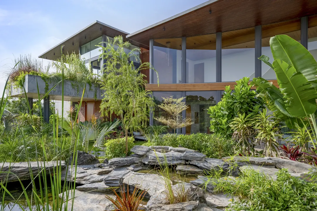 A rock-edged pond and layered planting in front of a glass house.