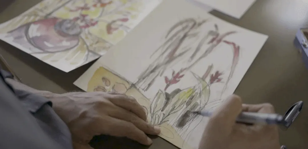 Hiren Patel's hands drawing plants on paper, seen from above.
