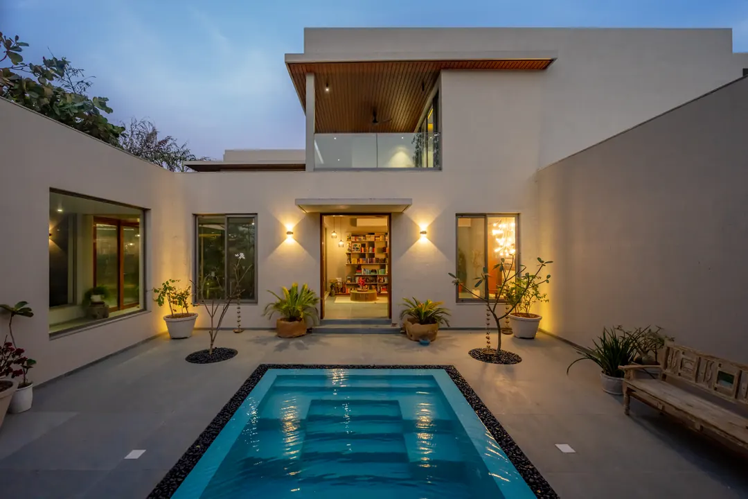 A long pool court lit at dusk, the house open on both sides.