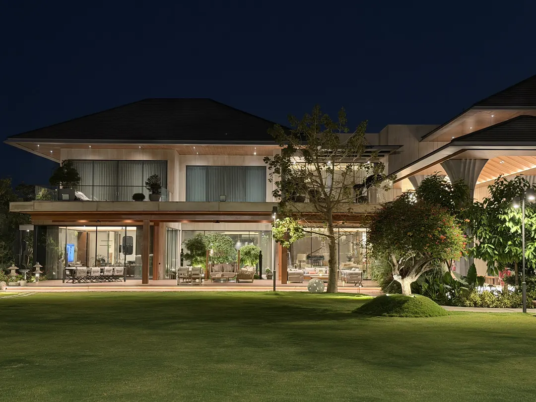 A lit house across the lawn at night, deep verandahs glowing.