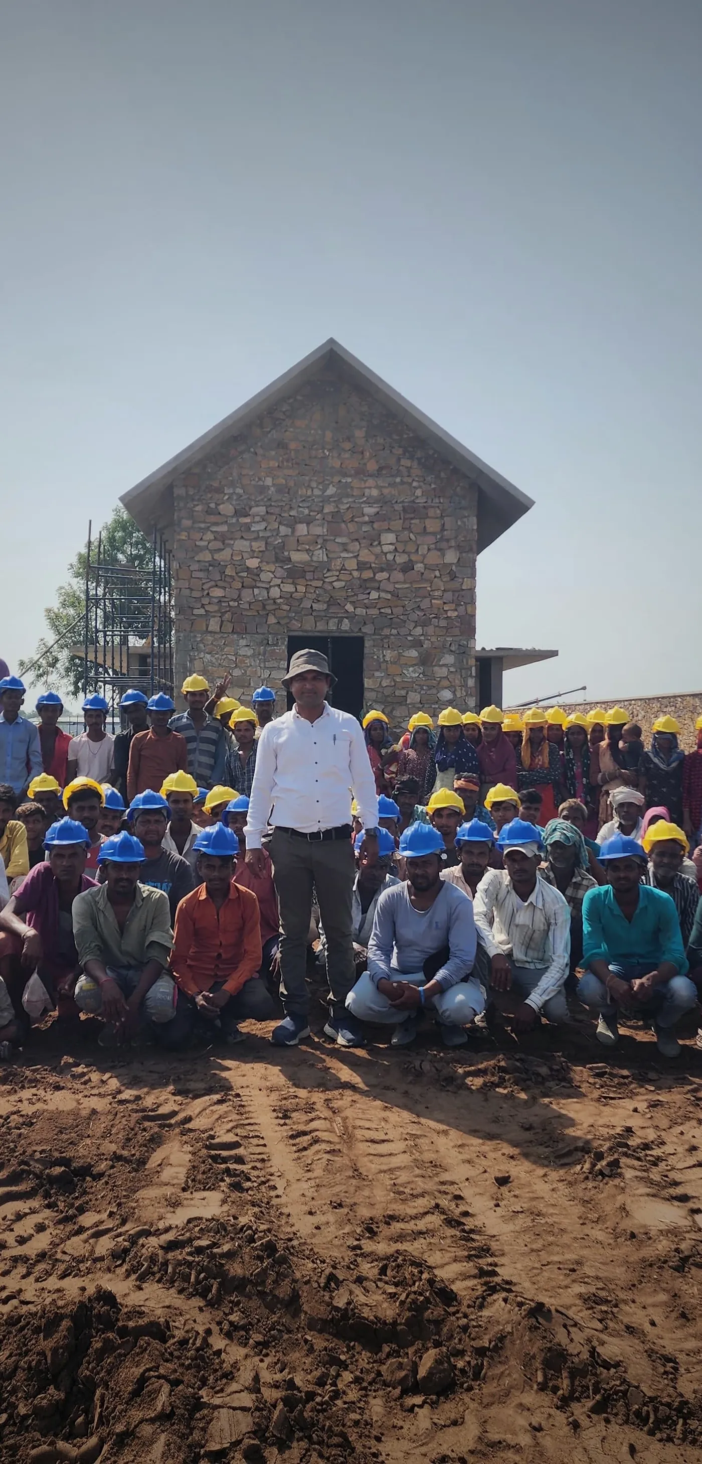 A site team in helmets, gathered in front of a finished stone house.