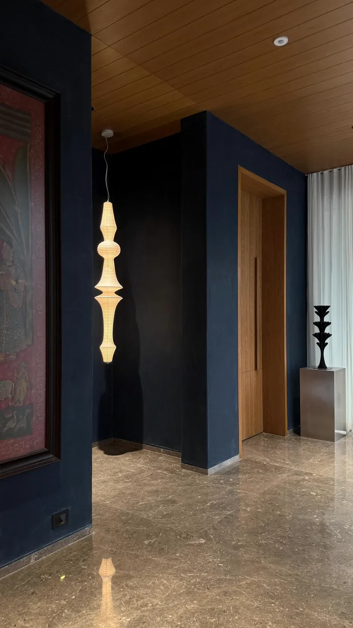An entrance in deep blue, a lit sculpture and a timber door.