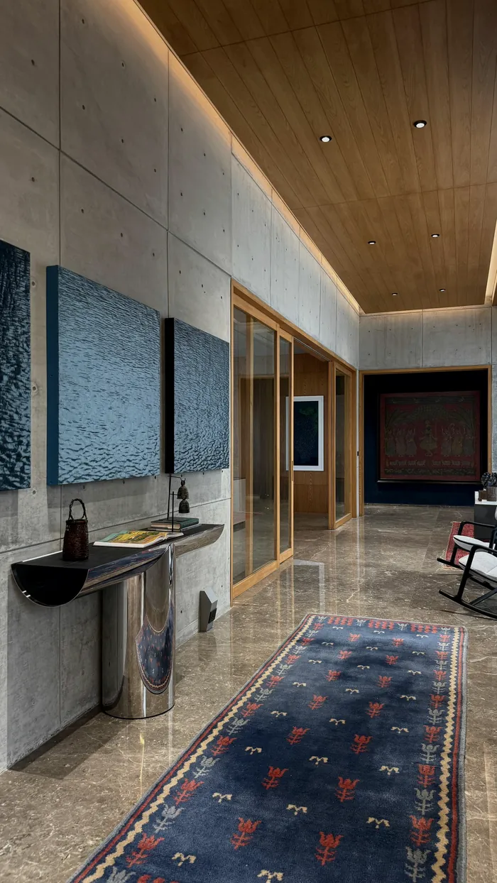 A gallery passage: paintings, a blue rug, a timber ceiling.