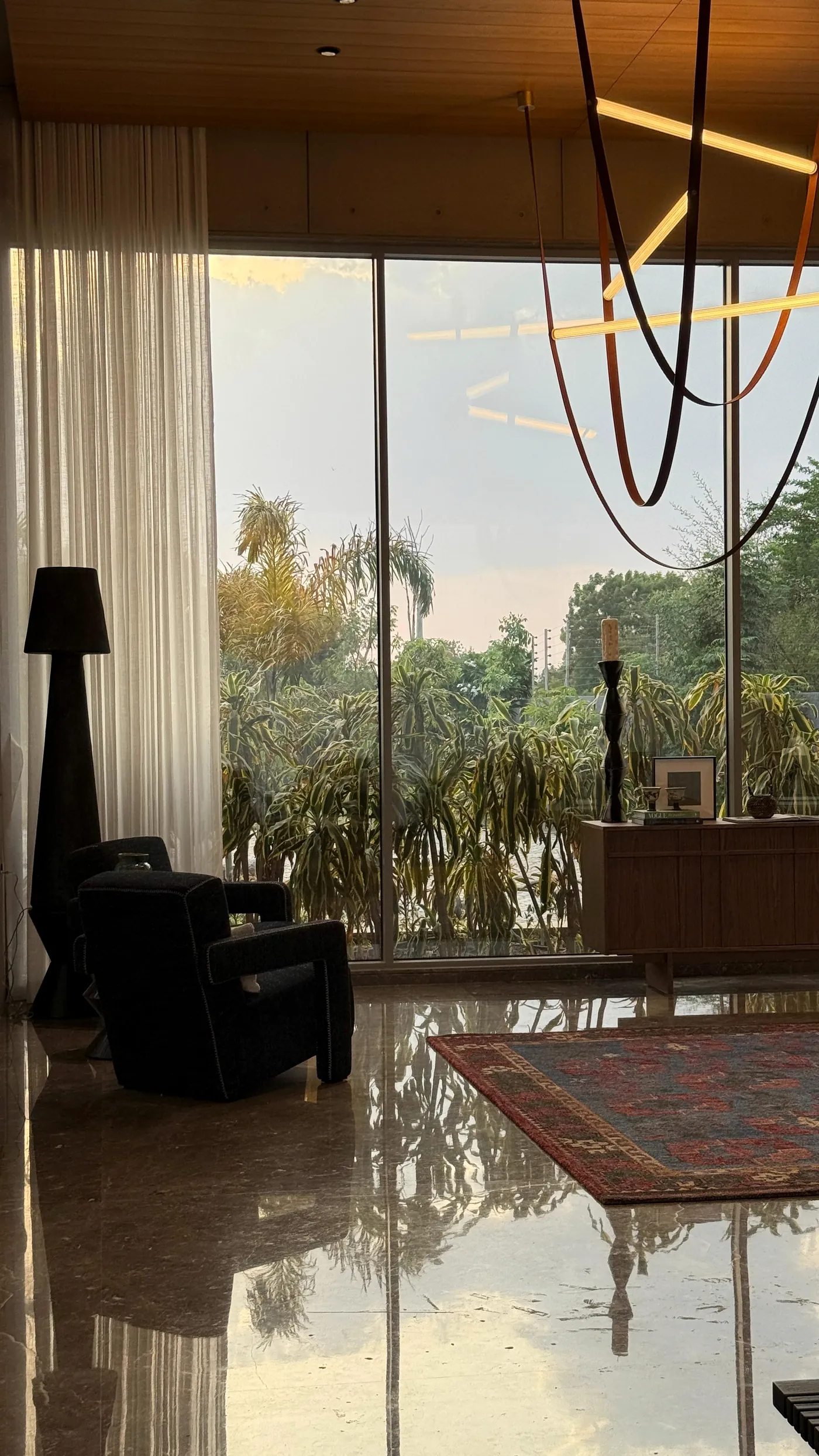 A room handed over: glass to the garden at dusk, an armchair and a rug on polished stone.