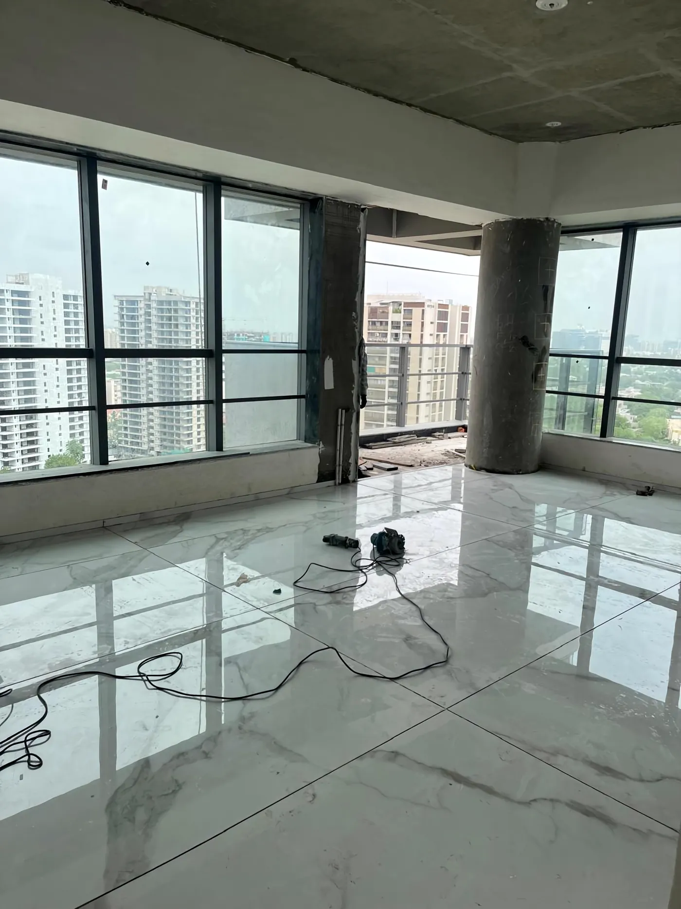 A room on site: glass to the city, the marble floor just laid, cables still across it.