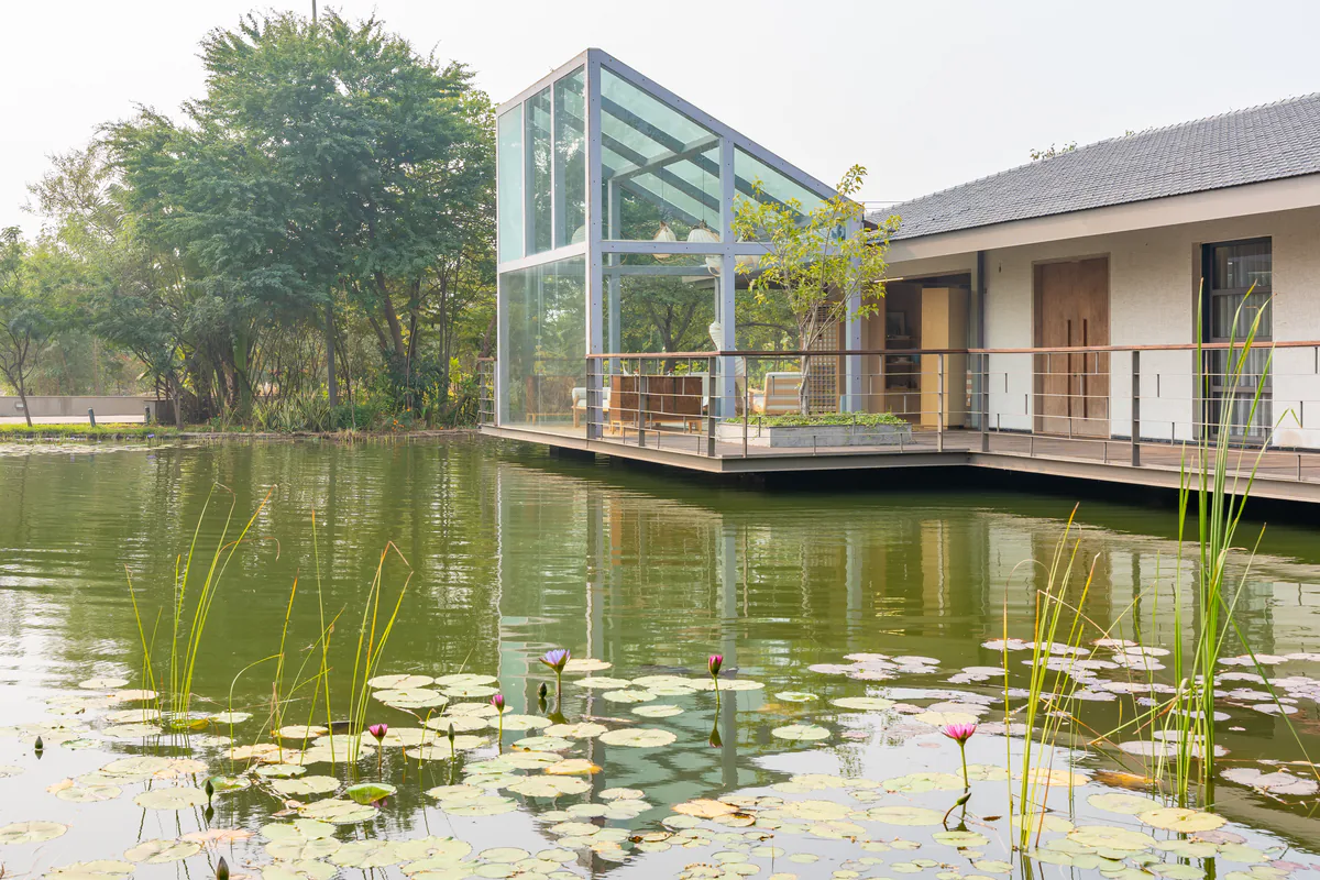 A glass gable pavilion and the tiled-roof lake house standing over a pond of pink water lilies.