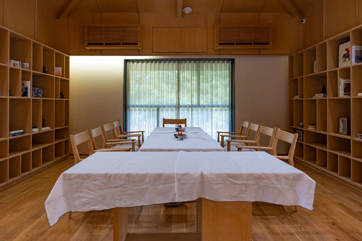 A long table dressed in white linen between two walls of timber shelves in the library, with a curtained window behind.